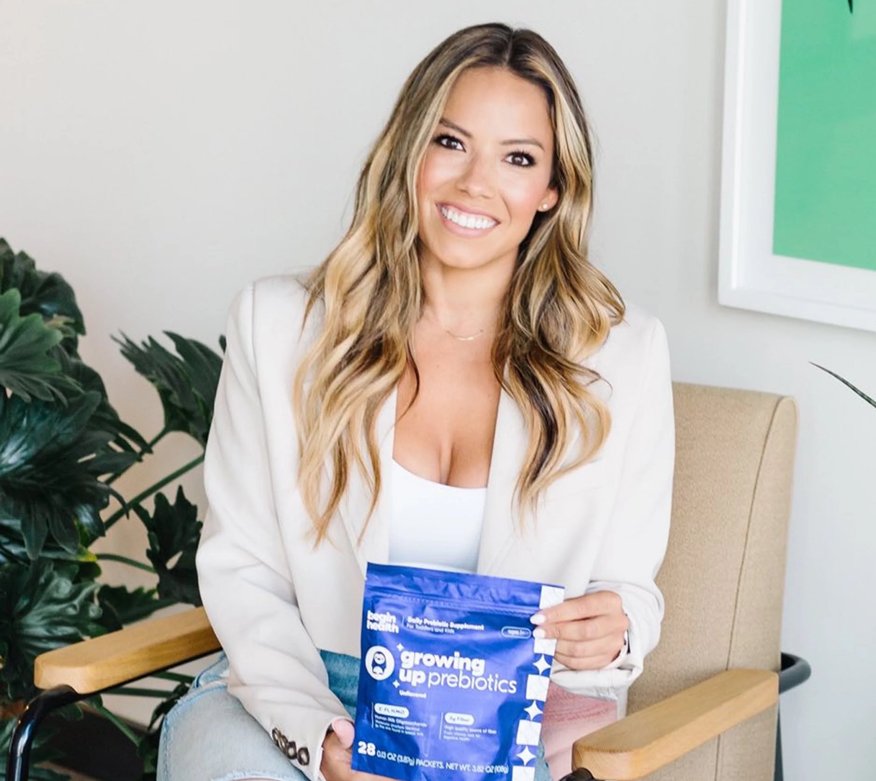 A woman seated holding a Begin Health prebiotics packet.