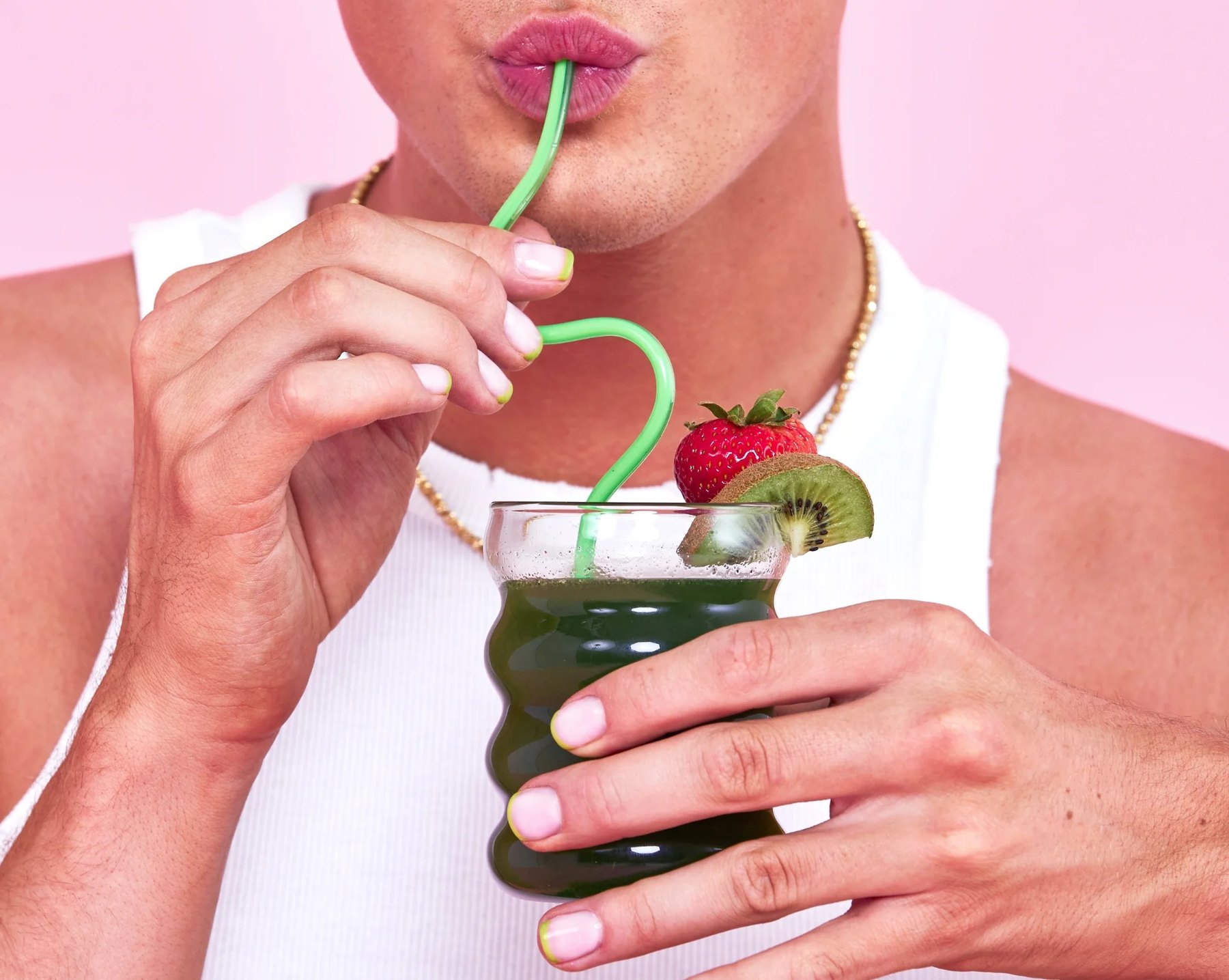 Woman sipping green Bloom drink with strawberry and kiwi garnish.