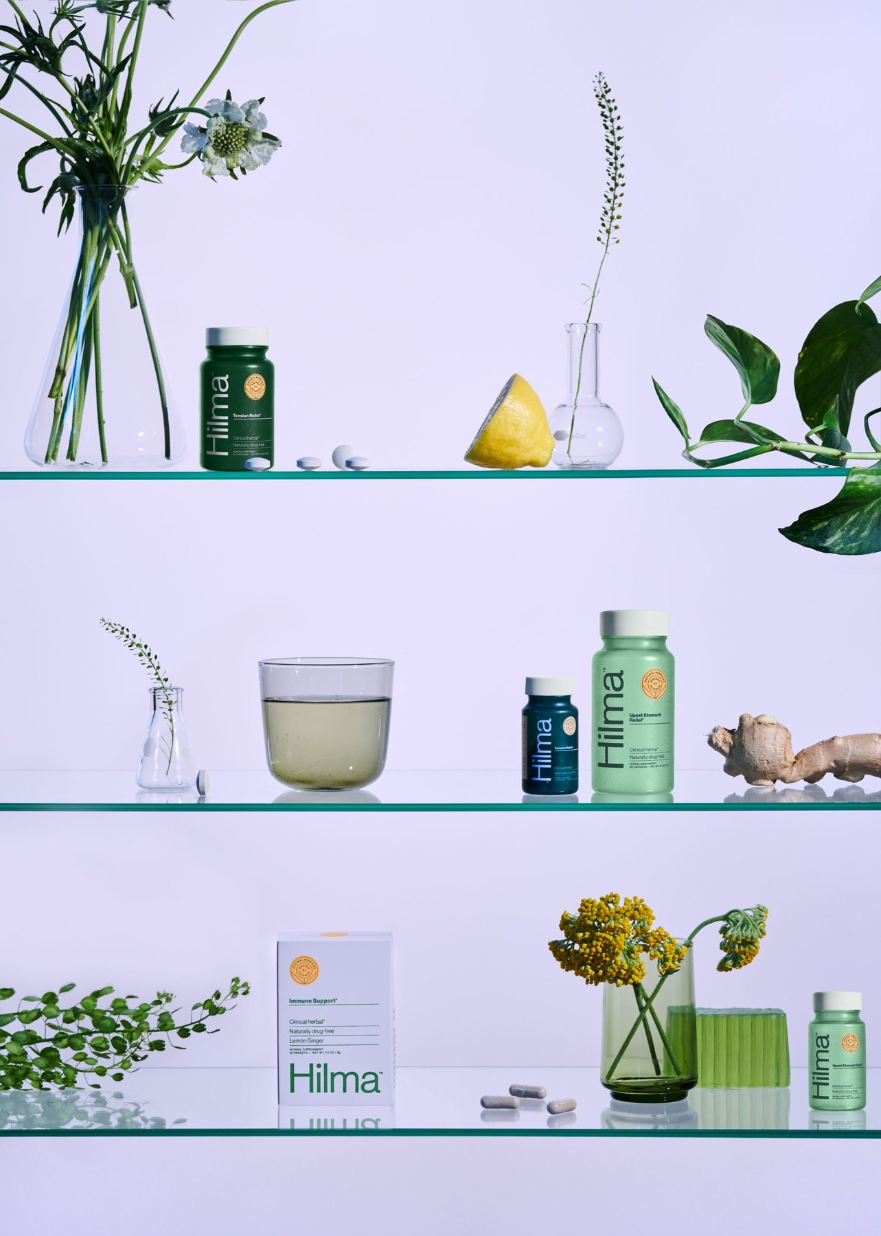 Hilma supplement bottles arranged on glass shelves with botanicals.