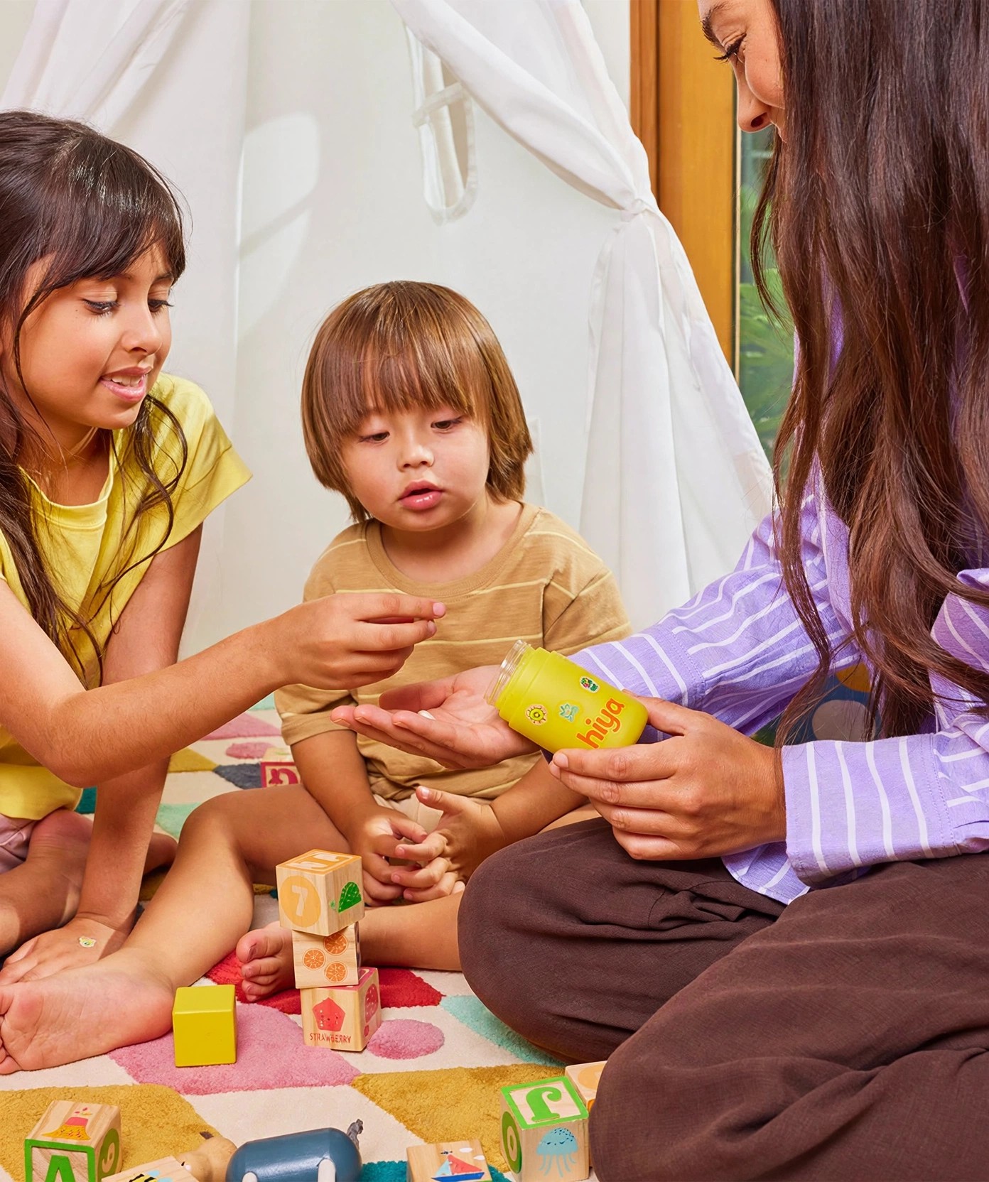 A woman gives a Hiya chewable to children playing with blocks.