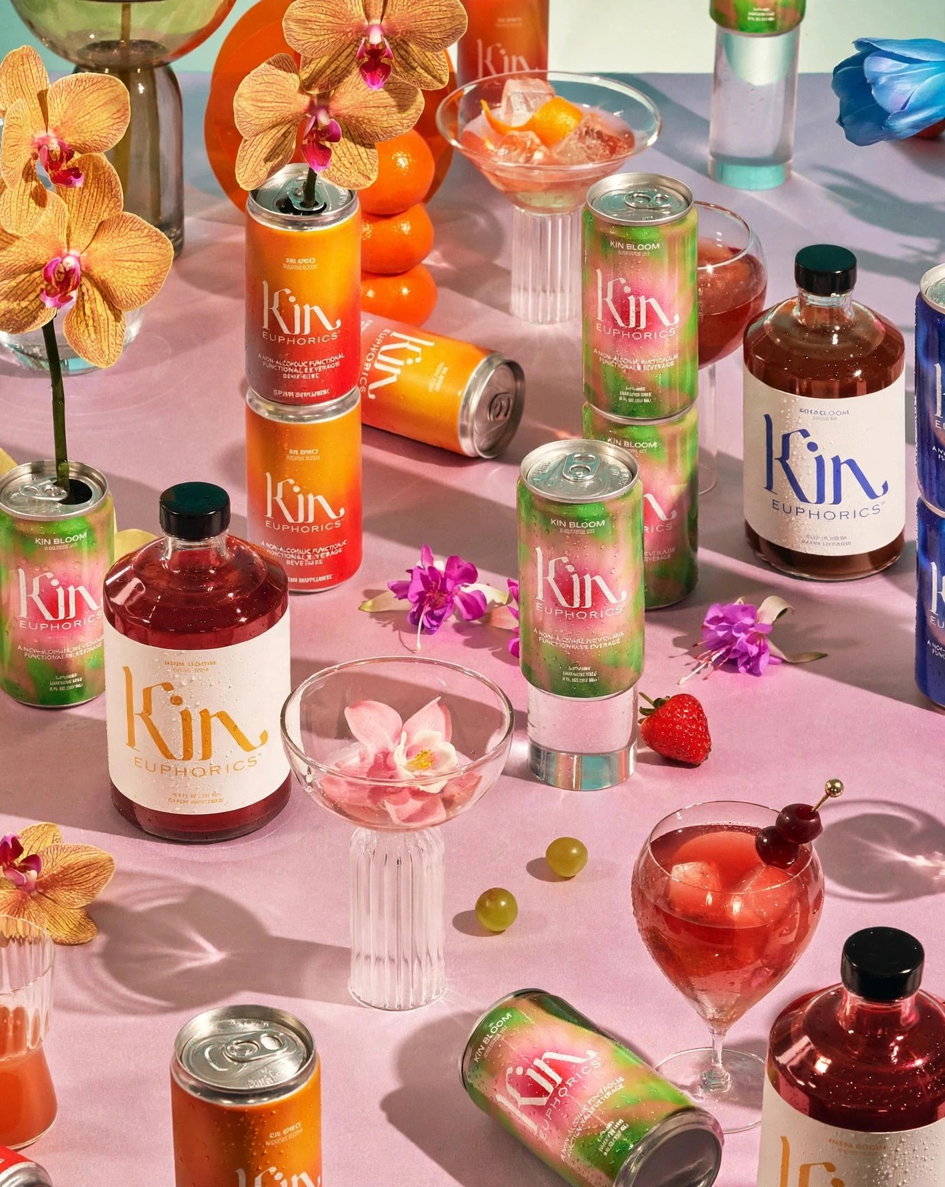 Kin cans and bottles on pink table with orchids and cocktails.