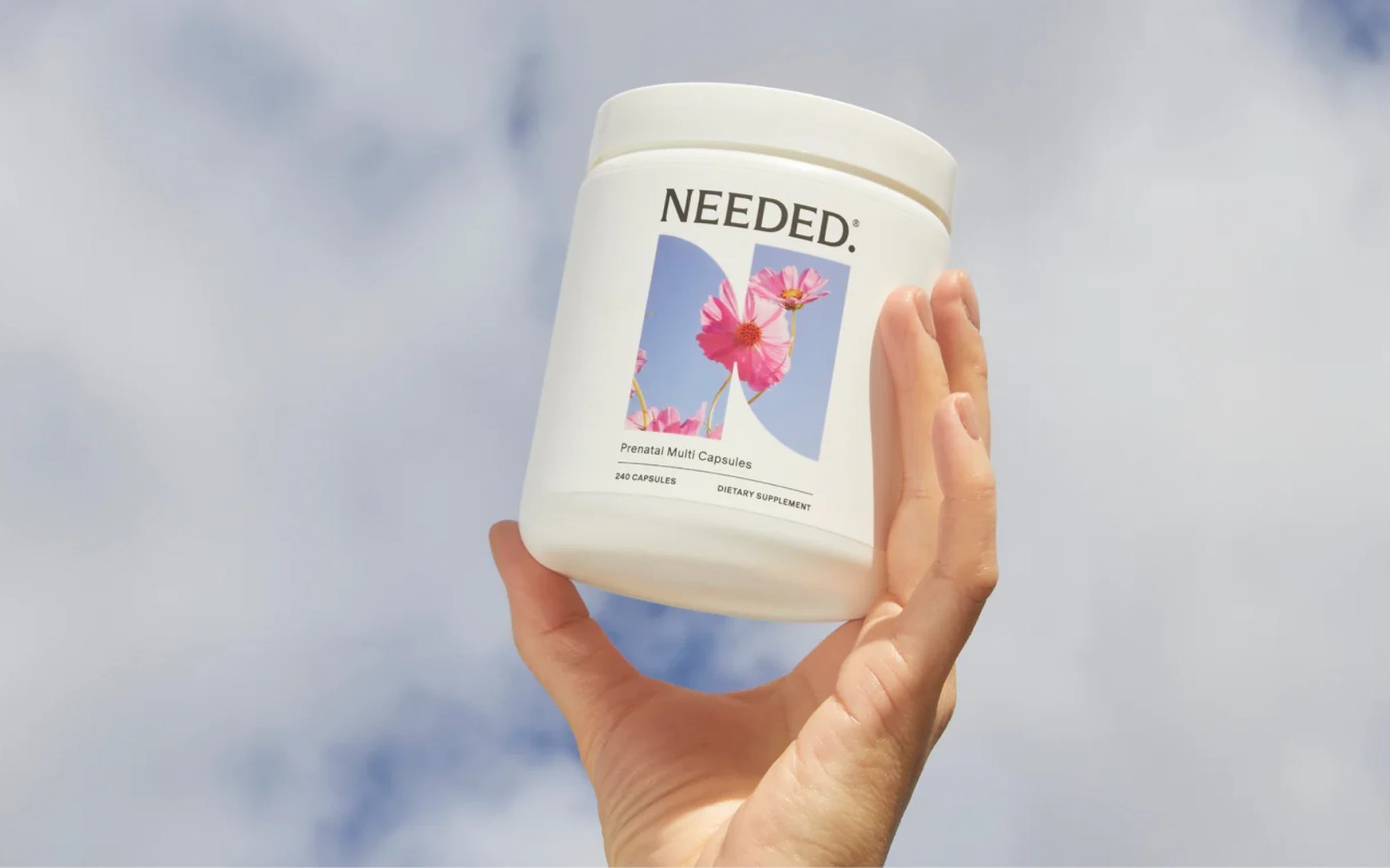 Hand holding Needed prenatal jar against cloudy sky.