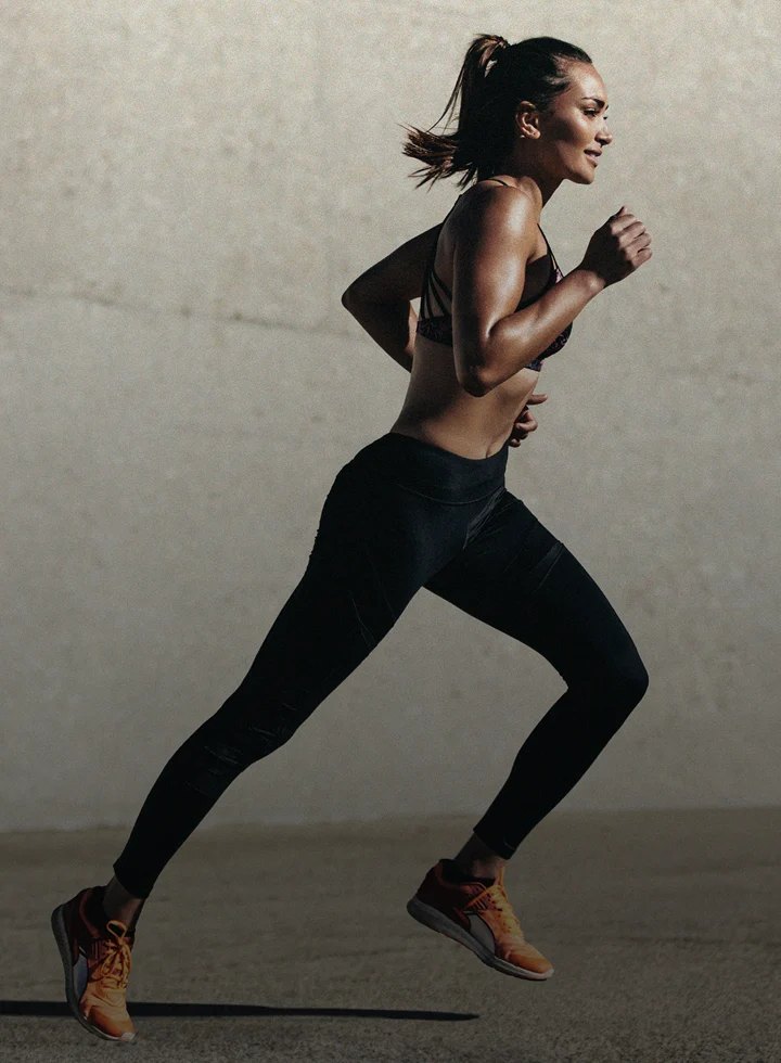Woman in athletic wear running outdoors against textured wall.