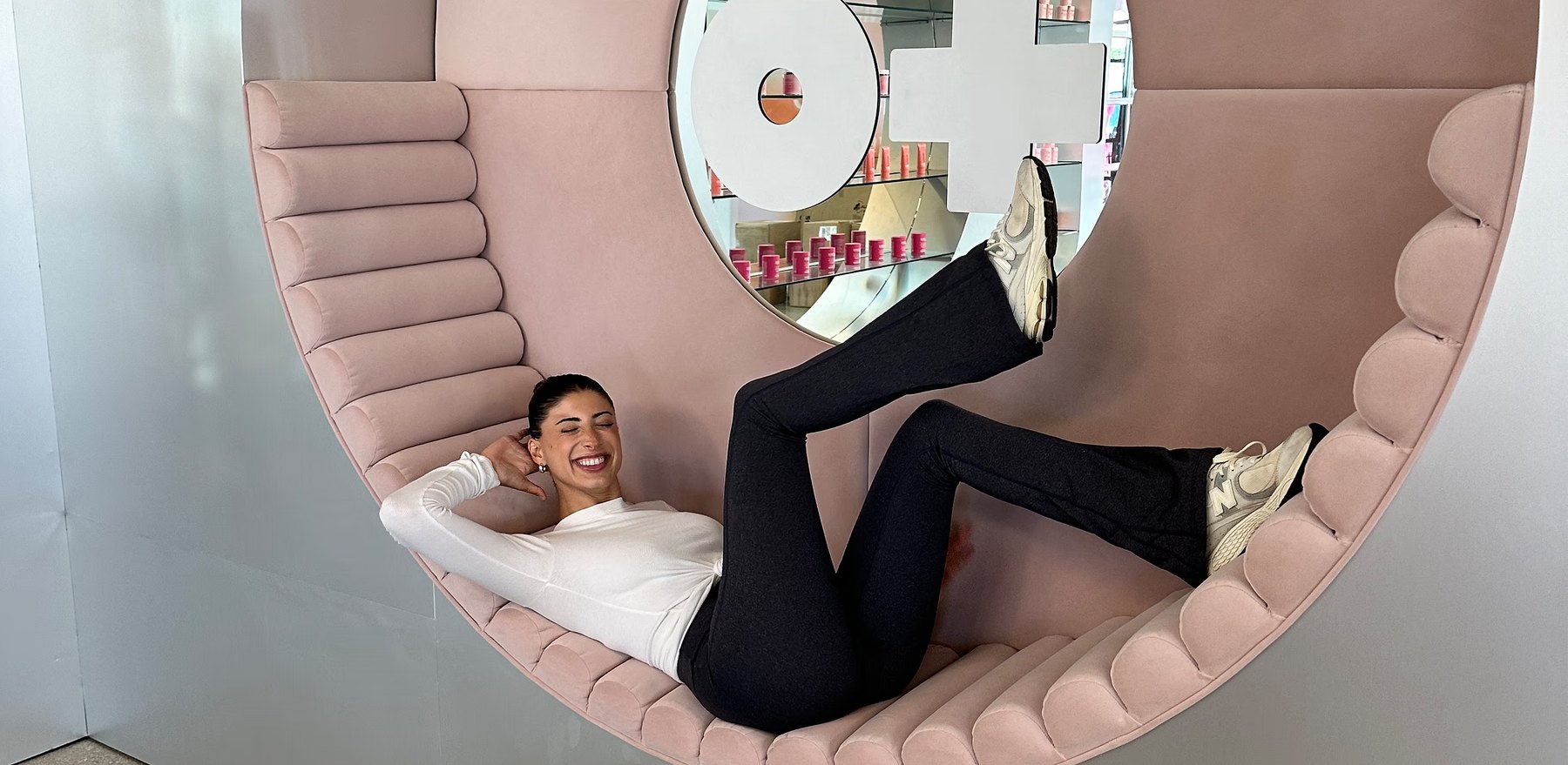 Brianna Bitton reclining on pink seating in a branded store.