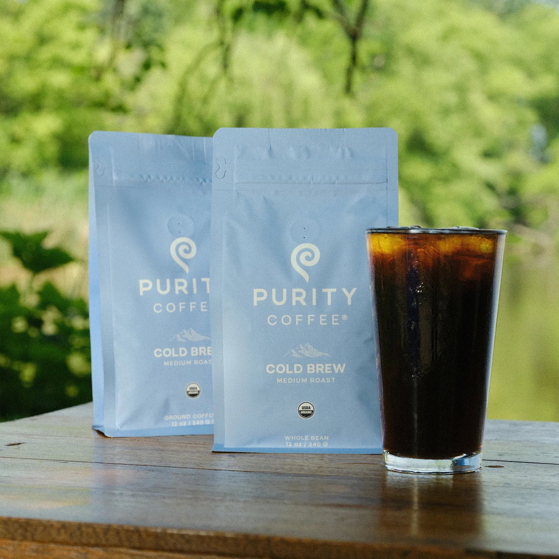 Two Purity Cold Brew bags beside a glass outdoors.