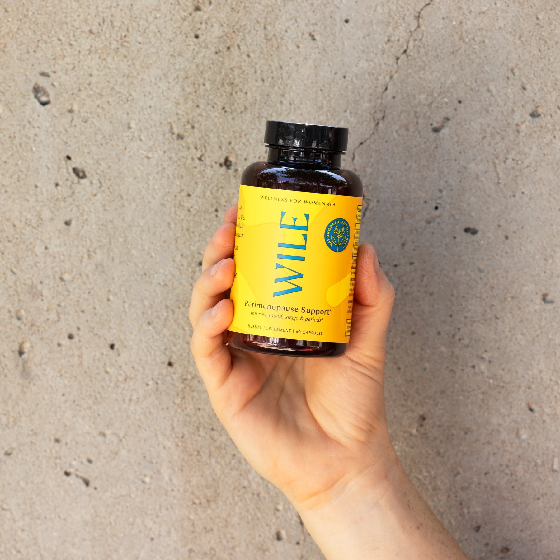 Hand holding Wile Perimenopause Support bottle against concrete wall.