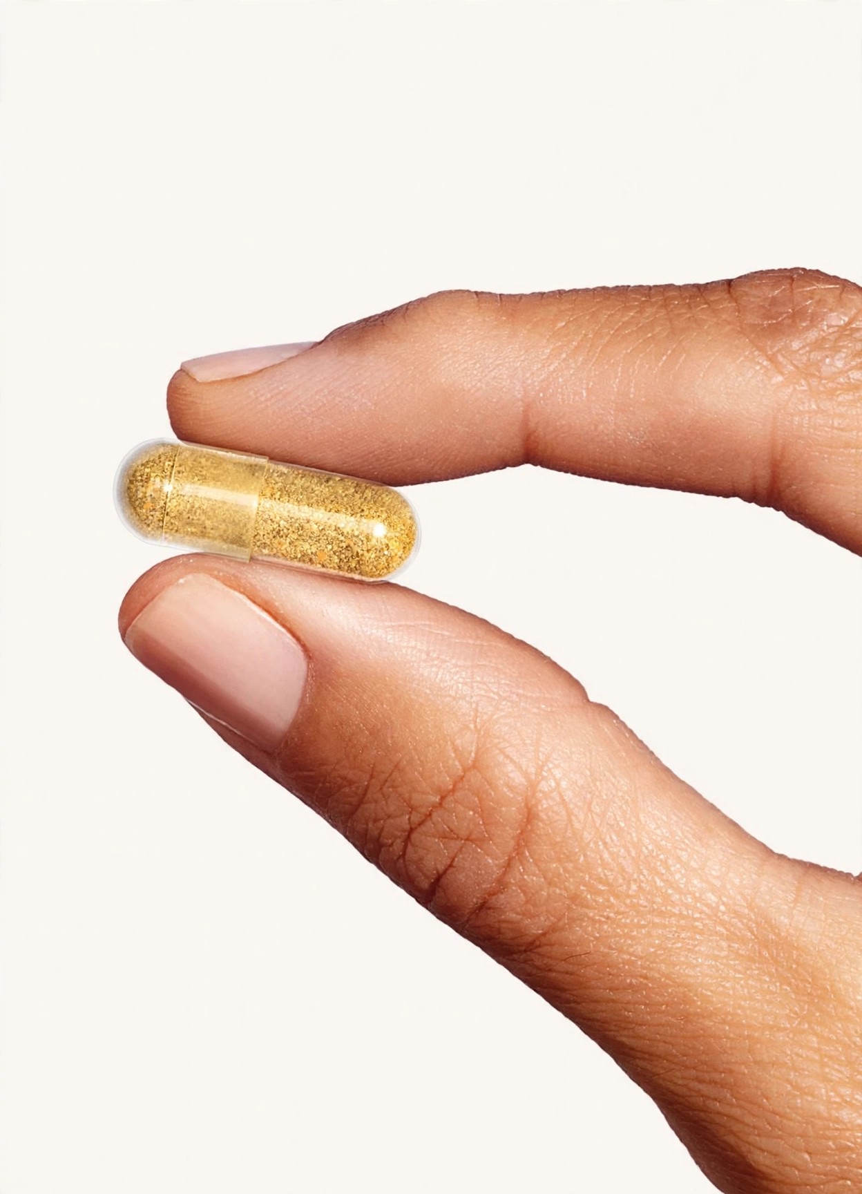 Fingers holding a translucent golden capsule against a plain background.