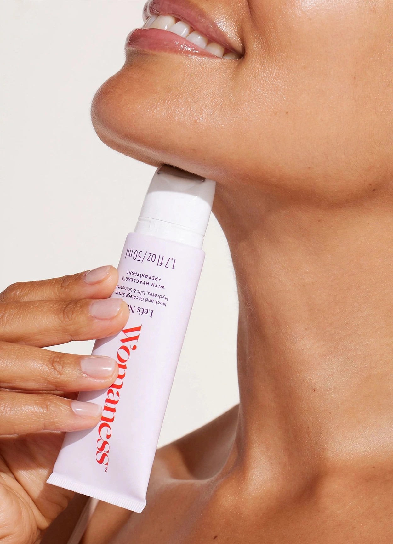 Hand holding Womaness neck serum tube to chin and neck.